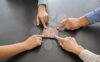 Business team assembling puzzle on dark table�