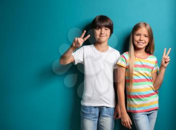 Boy and girl in t-shirts showing Victory gesture on color background�