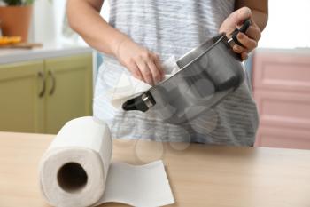 Woman wiping saucepan with paper towel in kitchen�