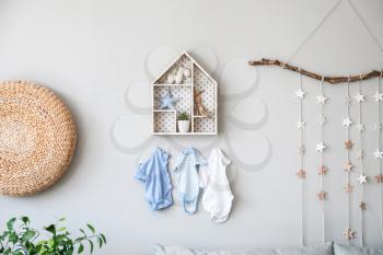 Stylish shelf with toys and clothes hanging on wall in children's room�