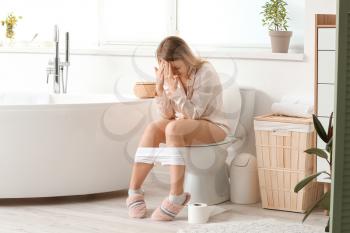 Young woman with hemorrhoids sitting on toilet bowl at home�