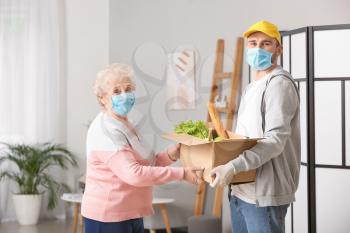 Senior woman receiving food from courier at home. Concept of epidemic�