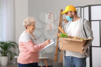 Senior woman receiving food from courier at home. Concept of epidemic�