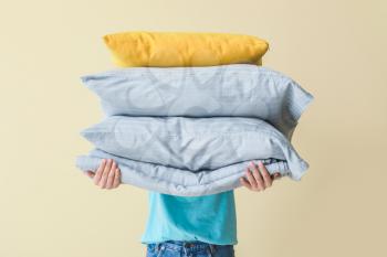 Woman holding pillows and bed sheets on color background�