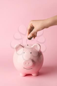 Woman putting money in piggy bank on color background�
