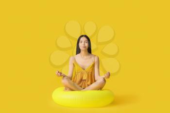 Meditating young woman with inflatable ring on color background�