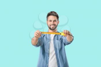 Young man with measuring tape on color background�