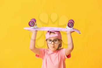 Cute little girl with skateboard on color background�
