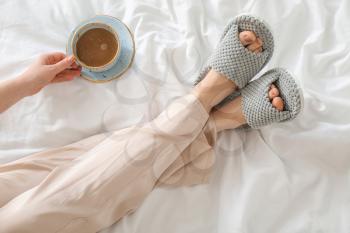 Woman in soft slippers drinking coffee in bedroom�