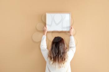 Woman hanging blank photo frame on wall�