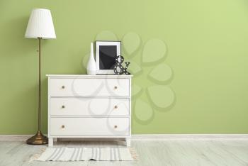 Modern chest of drawers with lamp near color wall in room�
