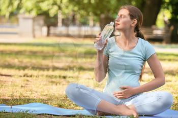Young pregnant woman drinking water while practicing yoga outdoors�