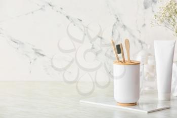 Holder with wooden toothbrushes and toothpaste on table in bathroom�