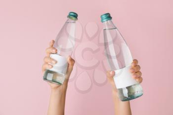 Hands with bottles of clean water on color background�