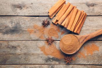 Spoon with cinnamon powder and sticks on wooden background�