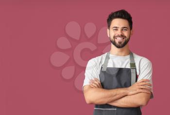 Young man wearing apron on color background�