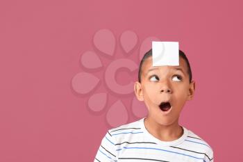 Little African-American boy with blank note paper on his forehead against color background�