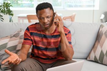 Stressed African-American man talking by phone at home�