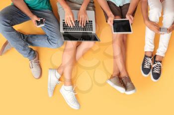 Teenagers with different devices on color background, top view�
