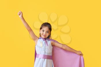 Little girl with golden ribbon wearing superhero costume on color background. Childhood cancer awareness concept�