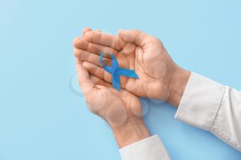 Male hands with blue ribbon on color background. Prostate cancer awareness concept�