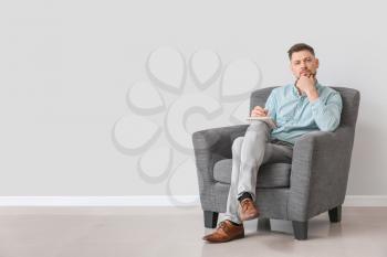 Male psychologist sitting in armchair near light wall�