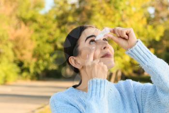 Young allergic woman using eye drops outdoors�