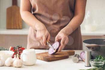 Woman cutting onion on table in kitchen�