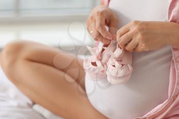 Pregnant young woman with baby shoes in bedroom�