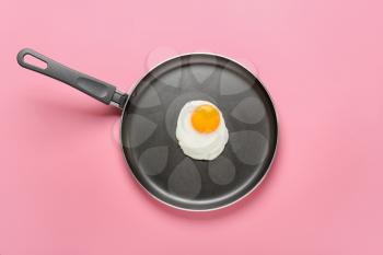 Frying pan with tasty egg on color background�
