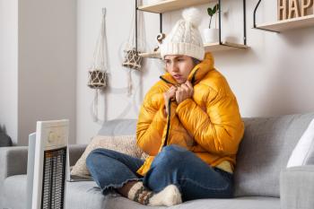 Young woman sitting near electric heater at home. Concept of heating season�