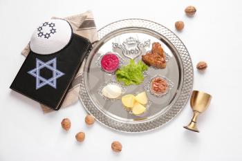 Passover Seder plate with traditional food, Torah and Jewish cap on white background�