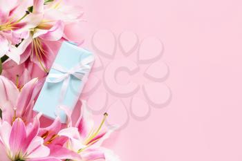 Beautiful lilies and gift on color background�