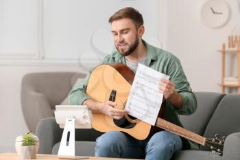 Young man taking music lessons online at home�