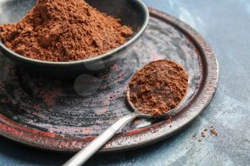 Bowl and spoon with cocoa powder on color background�