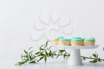 Dessert stand with tasty cupcakes and green branch on table�