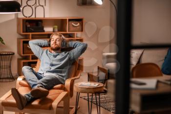 Young man listening to music while sitting in armchair at home�