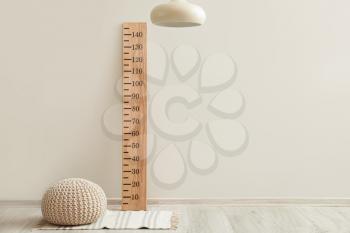 Wooden stadiometer and ottoman near light wall�