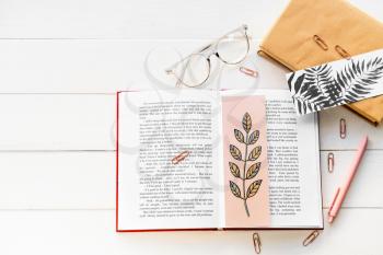 Books with bookmarks, glasses and stationery on light wooden background�