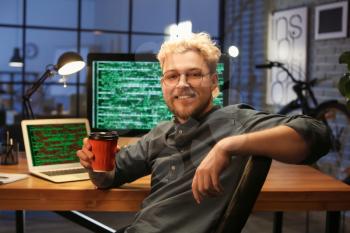 Young programmer drinking coffee in office at night�