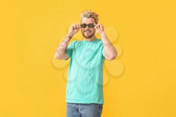 Young man with stylish sunglasses on color background�