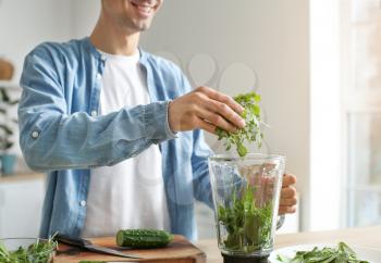 Young man preparing healthy green smoothie in kitchen�