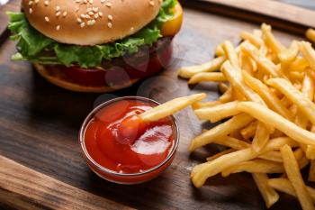 Tasty french fries, tomato sauce and burger on wooden board�