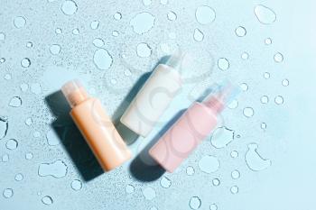 Bottles of cosmetic products on color background with water drops�