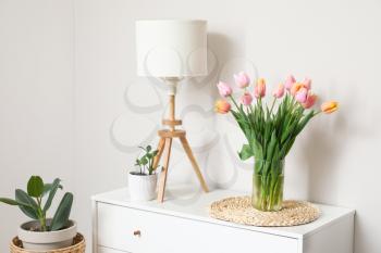 Bouquet of tulip flowers on chest of drawers near white wall�