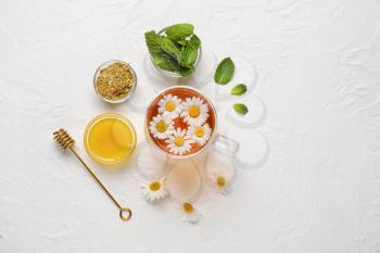 Composition with cup of chamomile tea, flowers, mint and honey on light background�