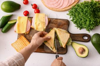 Woman cutting tasty sandwich on light background�