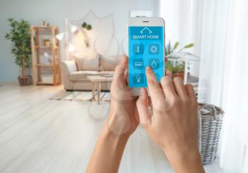 Woman using mobile phone application of smart home automation in room�