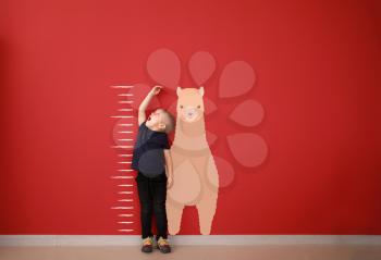 Surprised little boy measuring height near color wall�