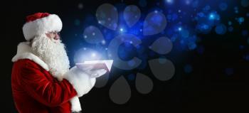 Santa Claus with magic book on dark background�